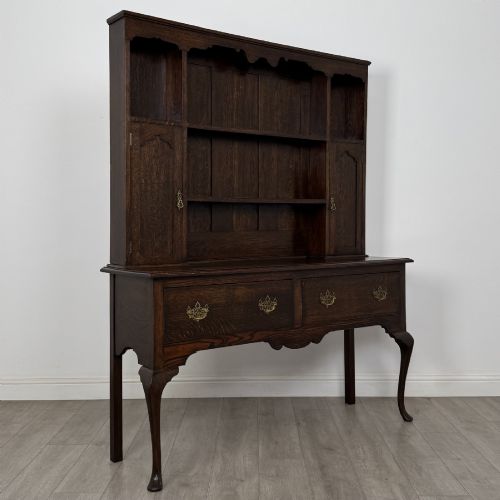 fig 7. A dark oak Queen Anne style dresser featuring an open-shelf upper rack with side cupboards above two drawers supported by cabriole legs.