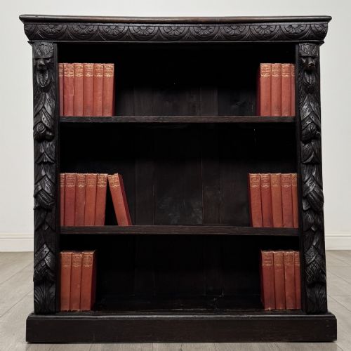 fig 1. A dark carved oak open bookcase featuring three shelf surfaces and pilasters detailed with foliate carvings and Green Man masks.