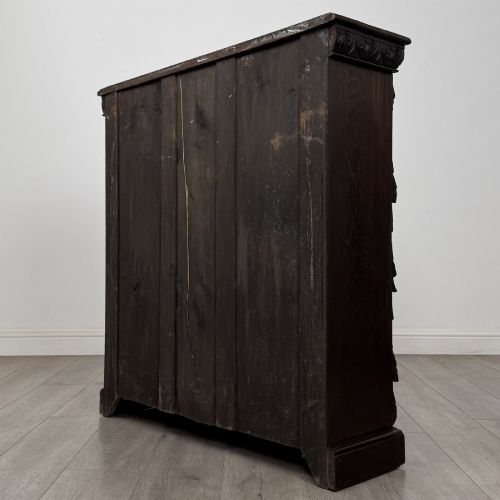 fig 6. A dark carved oak open bookcase featuring three shelf surfaces and pilasters detailed with foliate carvings and Green Man masks.
