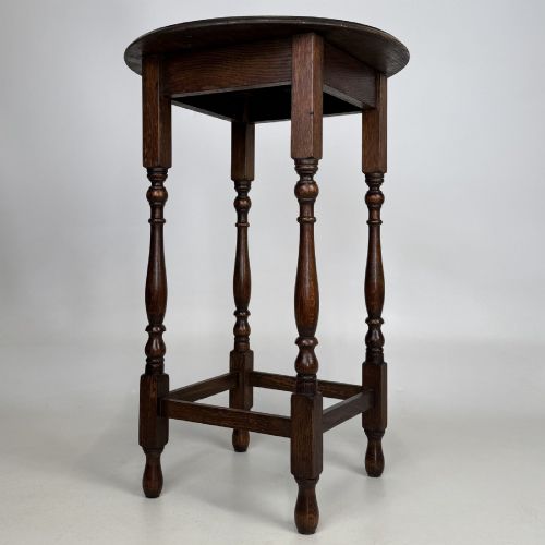 fig 2. A tall dark oak Jacobean style side table featuring a circular top, four slender turned baluster legs, and low square stretchers.