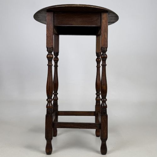 fig 3. A tall dark oak Jacobean style side table featuring a circular top, four slender turned baluster legs, and low square stretchers.