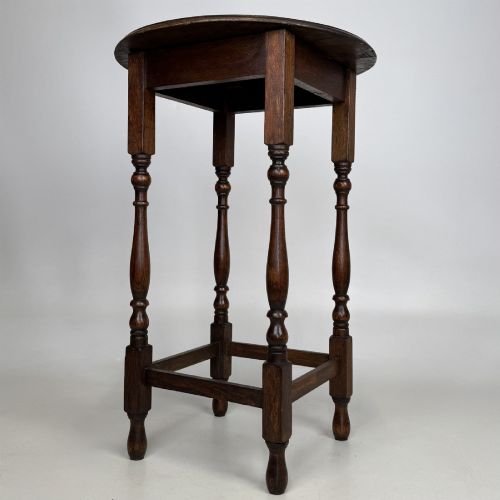 fig 4. A tall dark oak Jacobean style side table featuring a circular top, four slender turned baluster legs, and low square stretchers.
