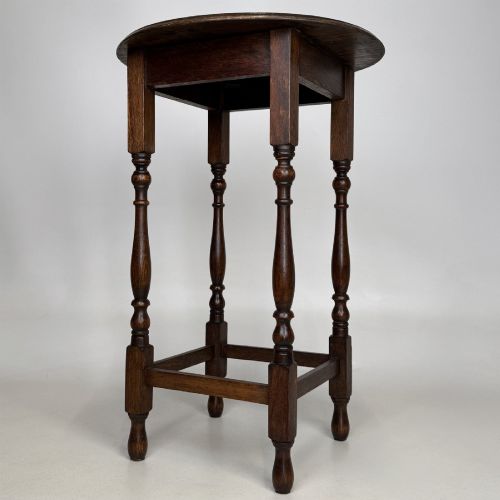 fig 5. A tall dark oak Jacobean style side table featuring a circular top, four slender turned baluster legs, and low square stretchers.