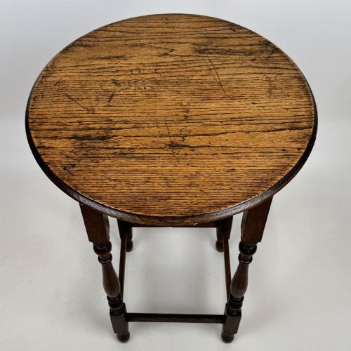 fig 6. A tall dark oak Jacobean style side table featuring a circular top, four slender turned baluster legs, and low square stretchers.
