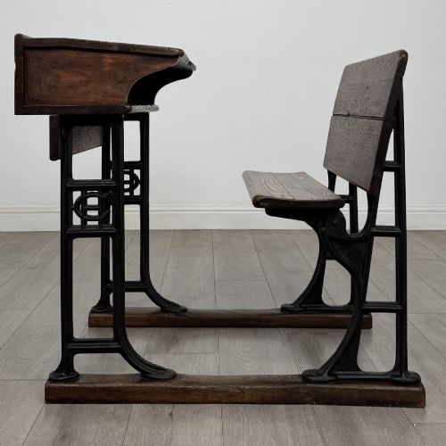 fig 1. An antique early 20th-century school desk featuring a sloped dark timber top with a storage compartment, attached to a black cast iron frame with an integrated bench seat.