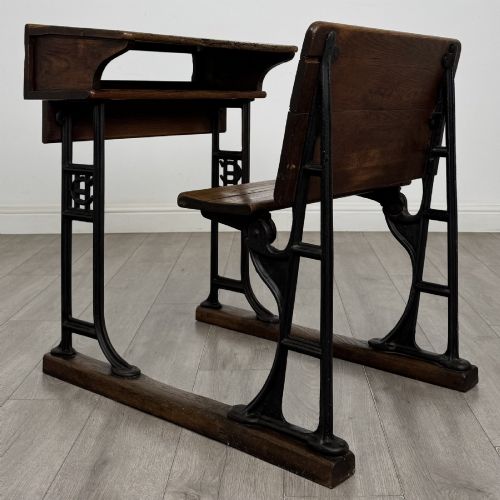 fig 2. An antique early 20th-century school desk featuring a sloped dark timber top with a storage compartment, attached to a black cast iron frame with an integrated bench seat.
