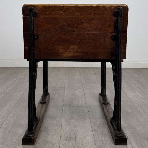 fig 3. An antique early 20th-century school desk featuring a sloped dark timber top with a storage compartment, attached to a black cast iron frame with an integrated bench seat.
