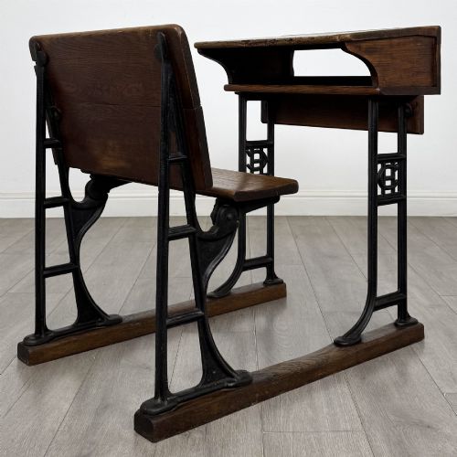 fig 4. An antique early 20th-century school desk featuring a sloped dark timber top with a storage compartment, attached to a black cast iron frame with an integrated bench seat.