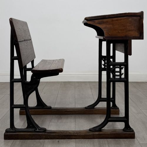 fig 5. An antique early 20th-century school desk featuring a sloped dark timber top with a storage compartment, attached to a black cast iron frame with an integrated bench seat.