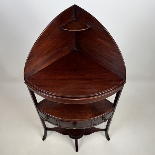 fig 4. A dark mahogany Georgian bow-front corner washstand featuring a curved splashback with a small upper shelf, a middle section with a central drawer flanked by dummy drawers, and splayed legs united by a circular stretcher.