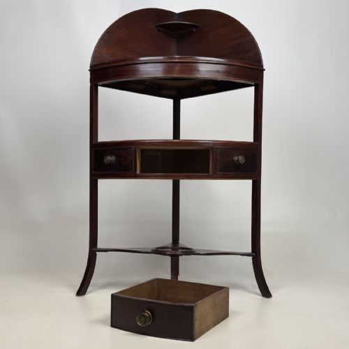 fig 5. A dark mahogany Georgian bow-front corner washstand featuring a curved splashback with a small upper shelf, a middle section with a central drawer flanked by dummy drawers, and splayed legs united by a circular stretcher.