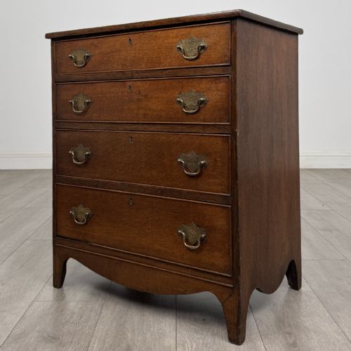 fig 1. A 19th-century oak chest of drawers featuring four graduated drawers with ornate brass backplate drop handles, keyhole escutcheons, and bracket feet.