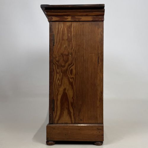 fig 2. A small Victorian pitch pine cupboard featuring twin panelled doors with pronounced wood grain, a moulded top, and a plinth base on small bun feet.