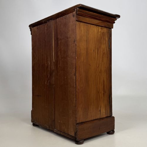 fig 5. A small Victorian pitch pine cupboard featuring twin panelled doors with pronounced wood grain, a moulded top, and a plinth base on small bun feet.