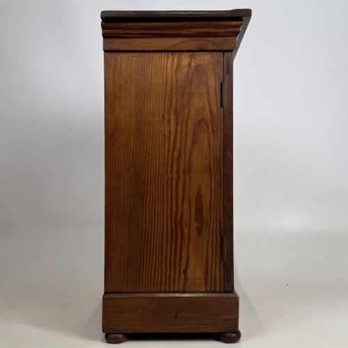 fig 6. A small Victorian pitch pine cupboard featuring twin panelled doors with pronounced wood grain, a moulded top, and a plinth base on small bun feet.