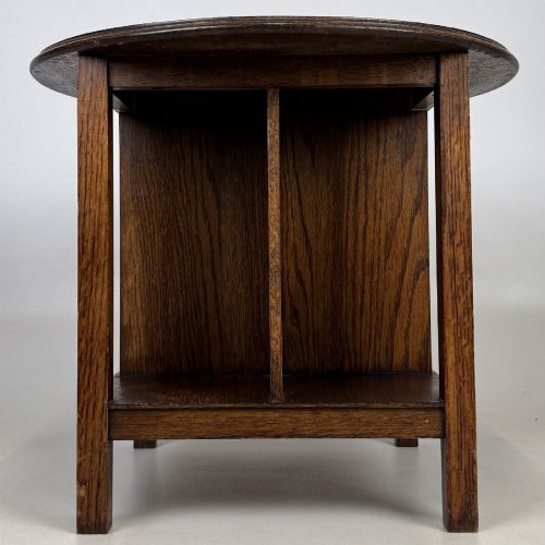 fig 1. An antique dark oak Arts and Crafts side table featuring a circular top, four square legs, and an integrated four-compartment book rack beneath.