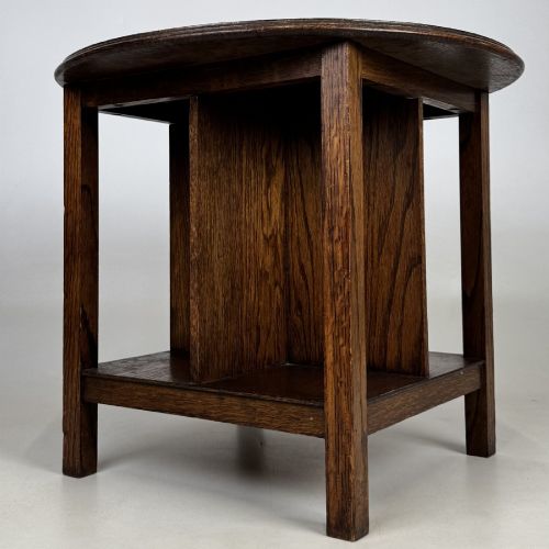 fig 2. An antique dark oak Arts and Crafts side table featuring a circular top, four square legs, and an integrated four-compartment book rack beneath.