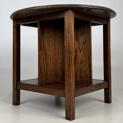 fig 4. An antique dark oak Arts and Crafts side table featuring a circular top, four square legs, and an integrated four-compartment book rack beneath.