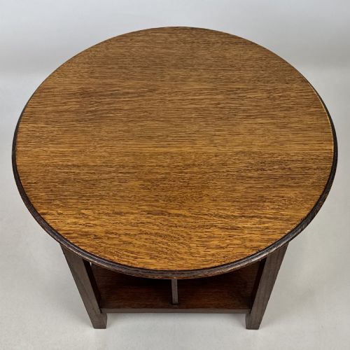 fig 5. An antique dark oak Arts and Crafts side table featuring a circular top, four square legs, and an integrated four-compartment book rack beneath.