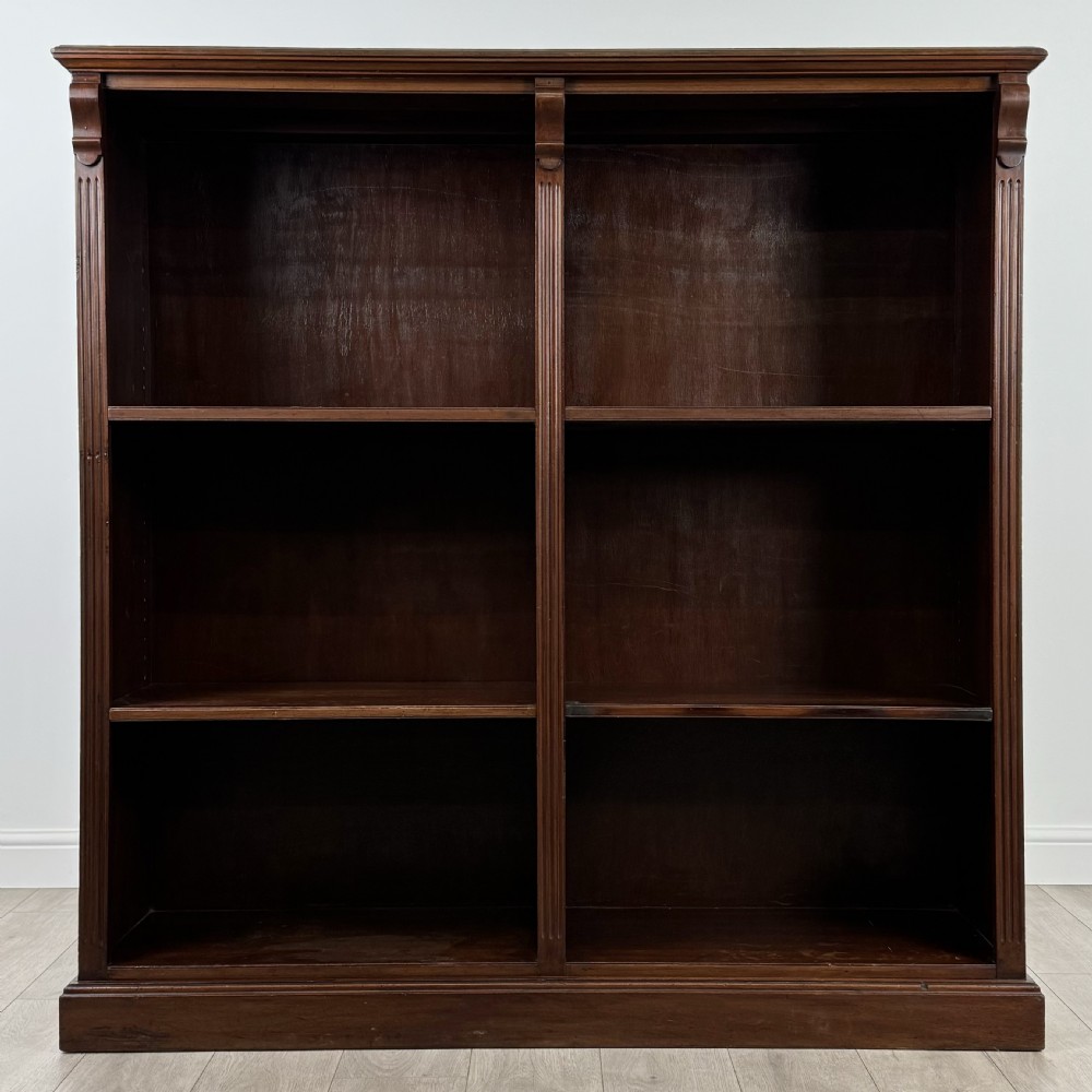 A front-facing view of a large, dark brown mahogany open bookcase featuring a central vertical divider and multiple fixed shelves.