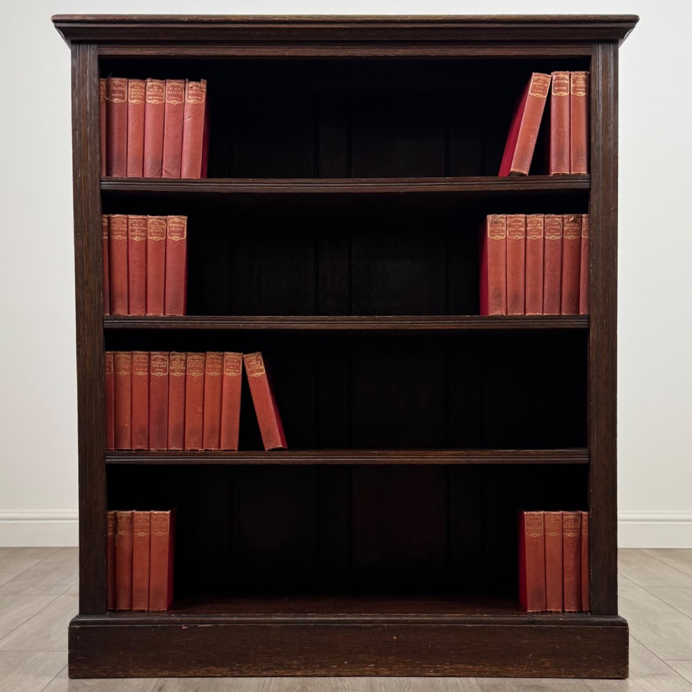 An antique dark oak open bookcase with four shelves containing rows of vintage books.