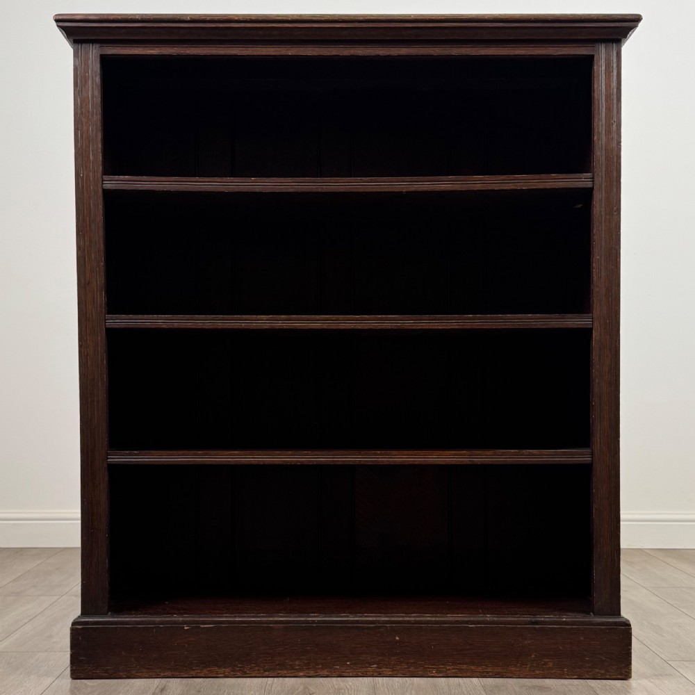 An antique dark oak open bookcase with four shelves containing rows of vintage books. View II