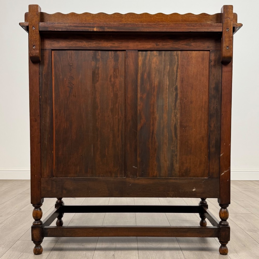 An antique twentieth-century golden oak cupboard featuring two panelled upper doors, a single lower drawer, and raised turned supports with an undertier shelf. View VII