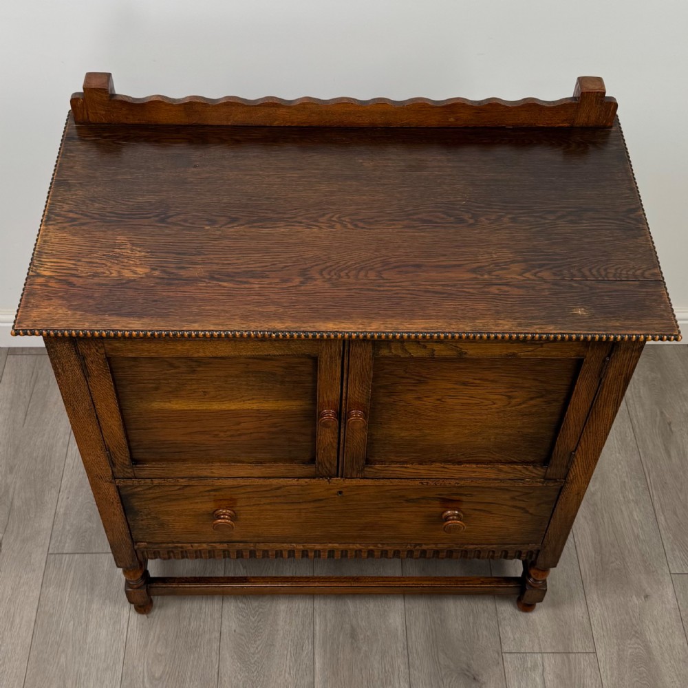 An antique twentieth-century golden oak cupboard featuring two panelled upper doors, a single lower drawer, and raised turned supports with an undertier shelf. View XI