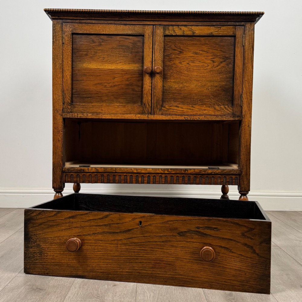 An antique twentieth-century golden oak cupboard featuring two panelled upper doors, a single lower drawer, and raised turned supports with an undertier shelf. View XII