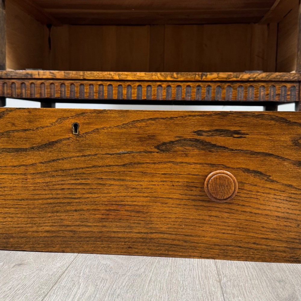 An antique twentieth-century golden oak cupboard featuring two panelled upper doors, a single lower drawer, and raised turned supports with an undertier shelf. View XIII
