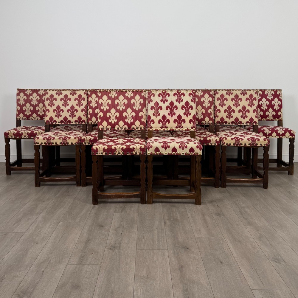 A set of fourteen dark oak dining chairs with red and cream fleur-de-lis patterned upholstery and brass stud trim.