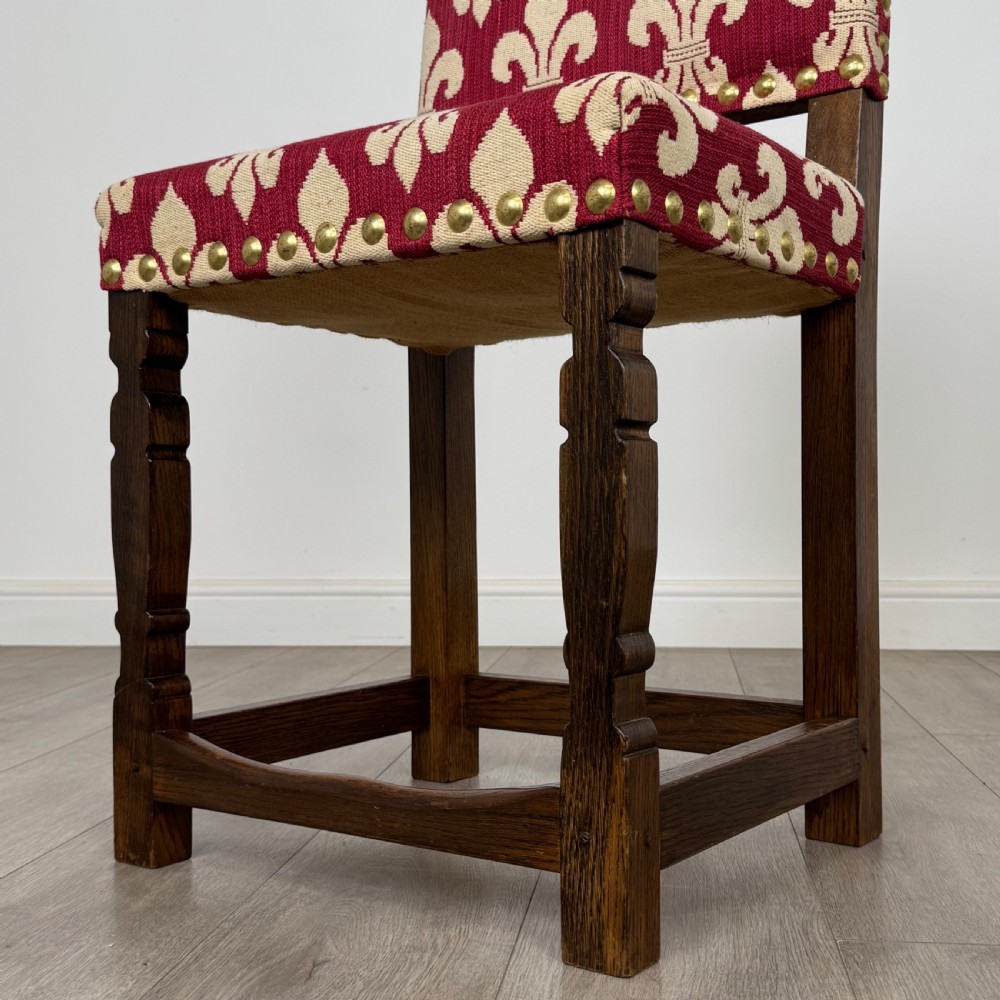 A set of fourteen dark oak dining chairs with red and cream fleur-de-lis patterned upholstery and brass stud trim. View V