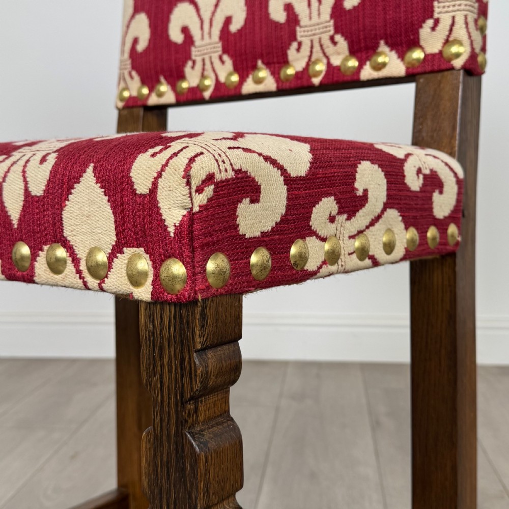 A set of fourteen dark oak dining chairs with red and cream fleur-de-lis patterned upholstery and brass stud trim. View VI