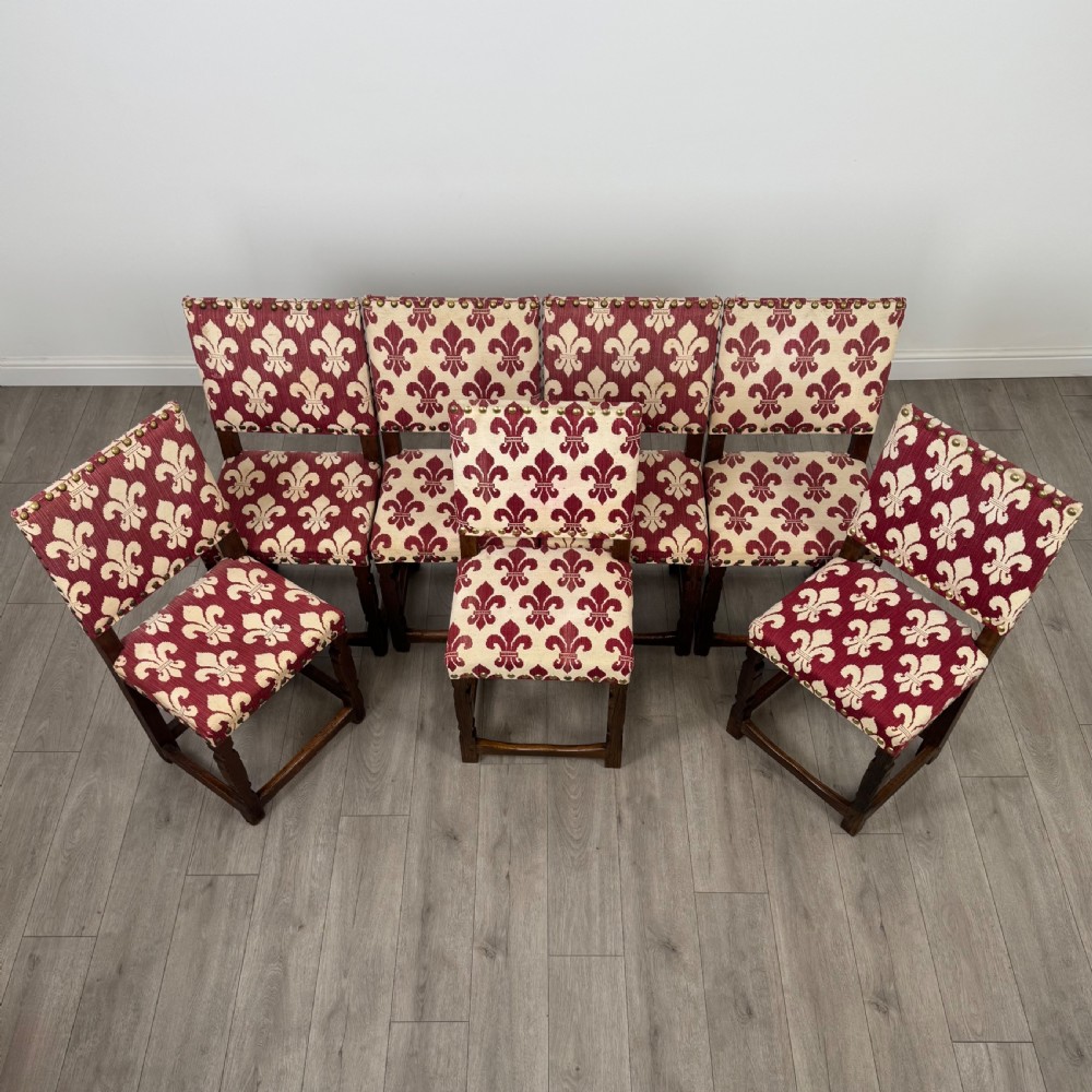 A set of fourteen dark oak dining chairs with red and cream fleur-de-lis patterned upholstery and brass stud trim. View X