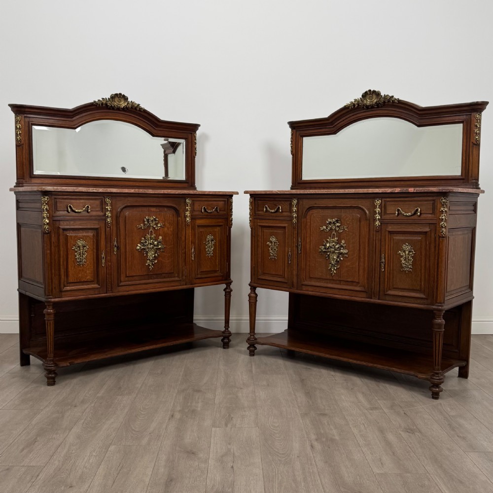 A pair of 19th-century French dark wood cabinets featuring pink marble tops, mirrored upper backs, gilded metal mounts, and lower open shelves.