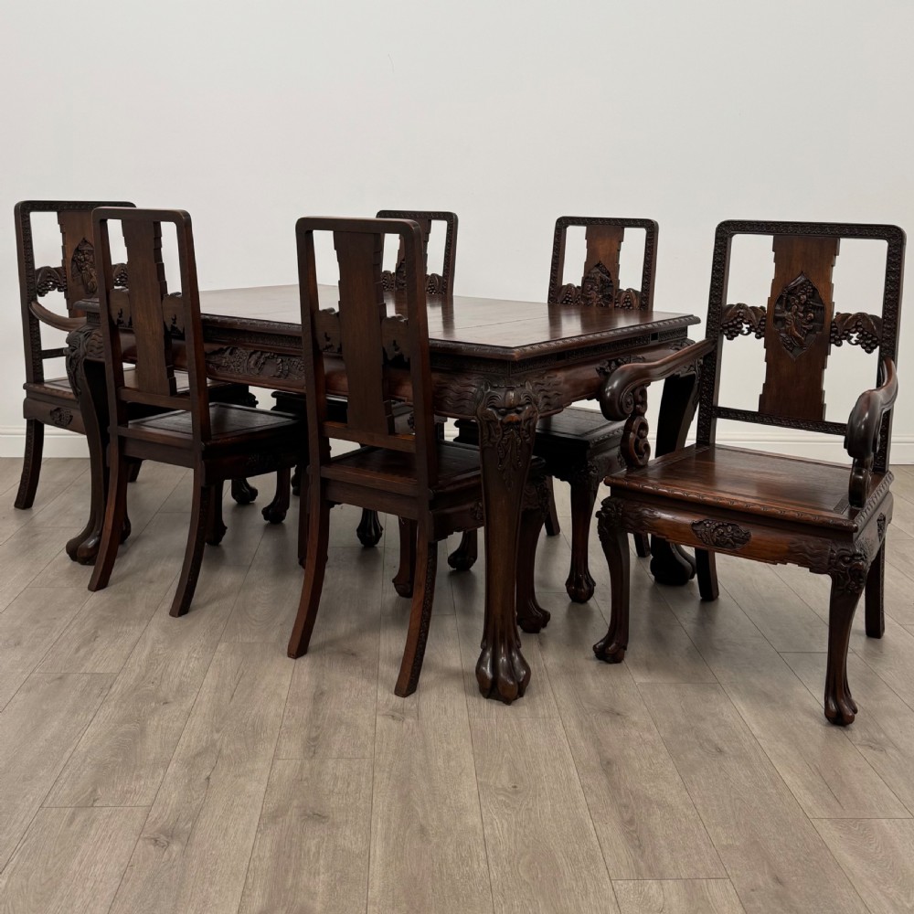 A dark carved rosewood dining suite featuring a rectangular table with carved cabriole legs accompanied by six splat-back chairs including two armchairs.