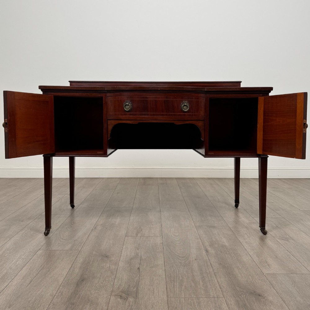 An Edwardian mahogany writing table featuring a central drawer, flanking cupboard doors, boxwood inlay, brass ring handles, and tapered legs on castors. View II