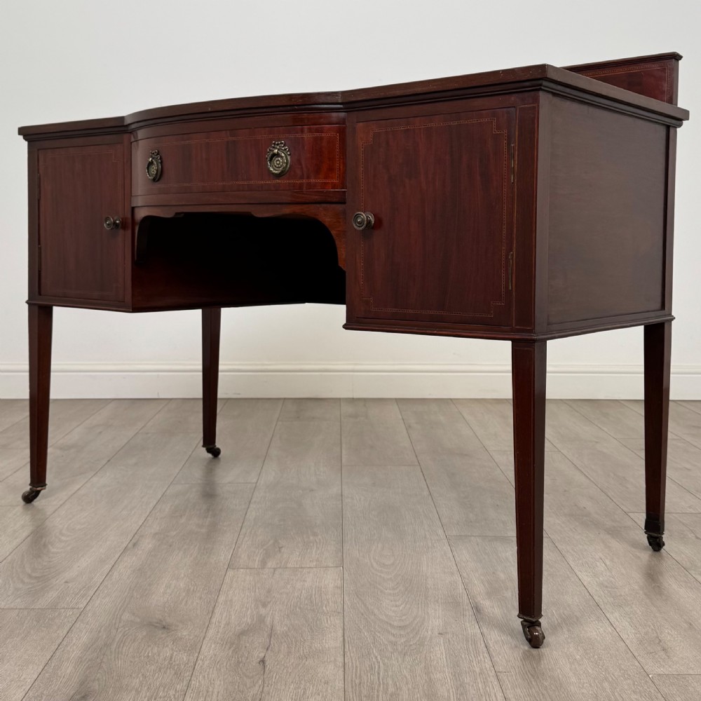 An Edwardian mahogany writing table featuring a central drawer, flanking cupboard doors, boxwood inlay, brass ring handles, and tapered legs on castors. View III