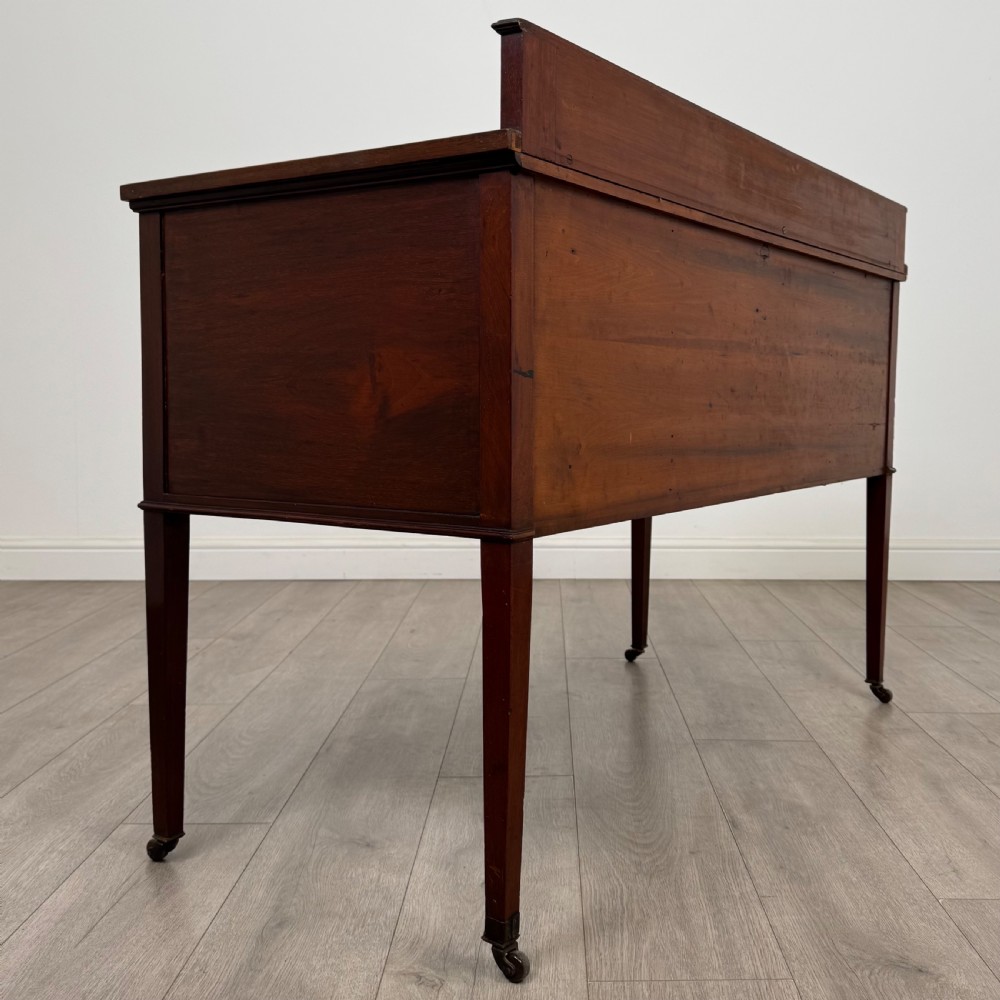 An Edwardian mahogany writing table featuring a central drawer, flanking cupboard doors, boxwood inlay, brass ring handles, and tapered legs on castors. View V
