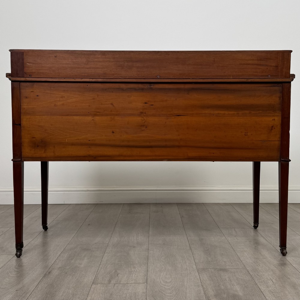 An Edwardian mahogany writing table featuring a central drawer, flanking cupboard doors, boxwood inlay, brass ring handles, and tapered legs on castors. View VI