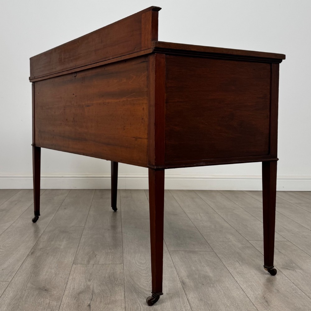 An Edwardian mahogany writing table featuring a central drawer, flanking cupboard doors, boxwood inlay, brass ring handles, and tapered legs on castors. View VII