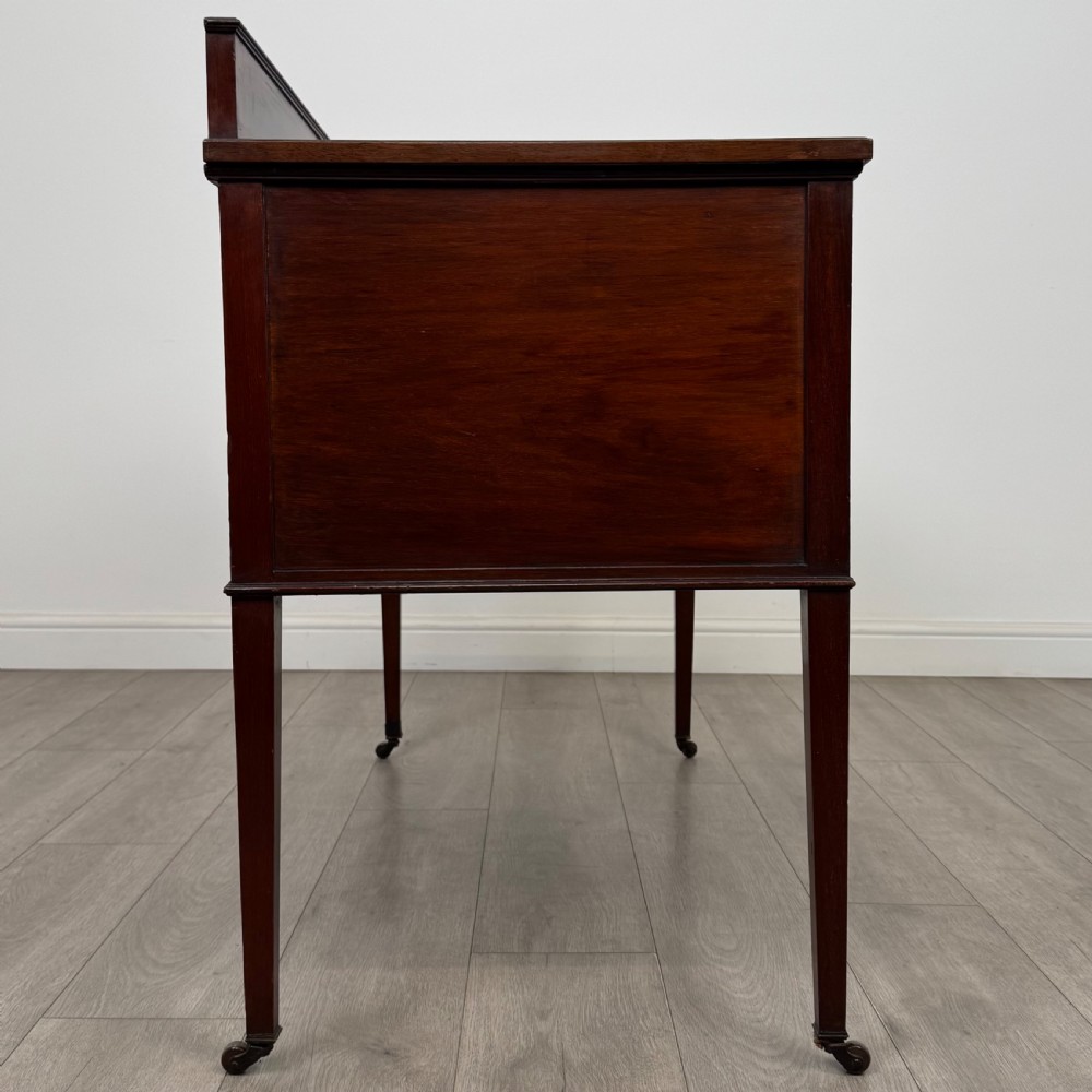 An Edwardian mahogany writing table featuring a central drawer, flanking cupboard doors, boxwood inlay, brass ring handles, and tapered legs on castors. View VIII