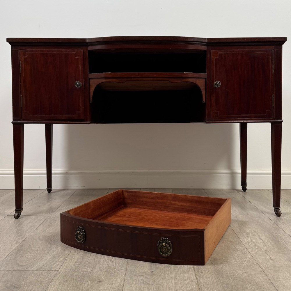 An Edwardian mahogany writing table featuring a central drawer, flanking cupboard doors, boxwood inlay, brass ring handles, and tapered legs on castors. View XI