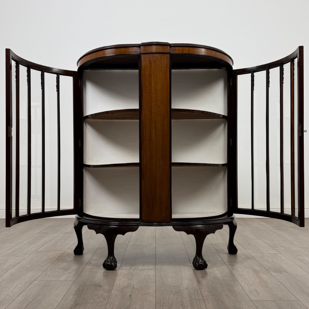 An early twentieth-century mahogany bow-front display cabinet featuring curved glass doors, vertical glazing bars, internal shelves, and cabriole legs with ball-and-claw feet. View II