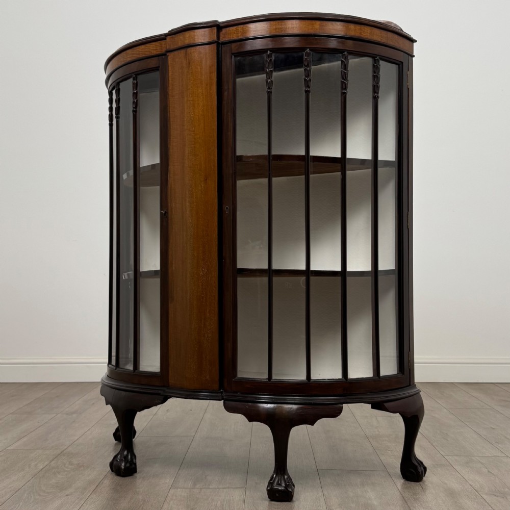 An early twentieth-century mahogany bow-front display cabinet featuring curved glass doors, vertical glazing bars, internal shelves, and cabriole legs with ball-and-claw feet. View III