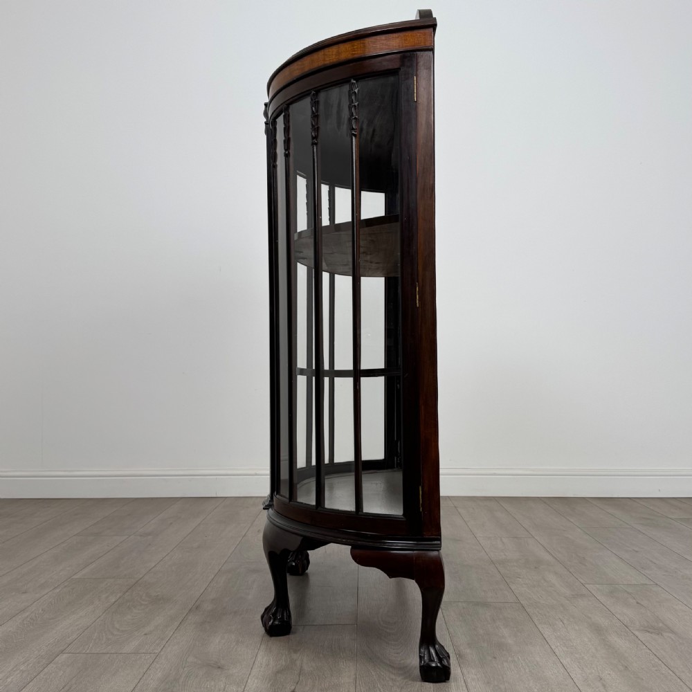 An early twentieth-century mahogany bow-front display cabinet featuring curved glass doors, vertical glazing bars, internal shelves, and cabriole legs with ball-and-claw feet. View IV