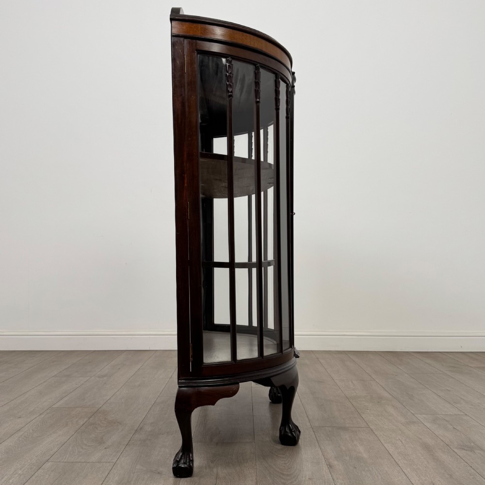 An early twentieth-century mahogany bow-front display cabinet featuring curved glass doors, vertical glazing bars, internal shelves, and cabriole legs with ball-and-claw feet. View VIII