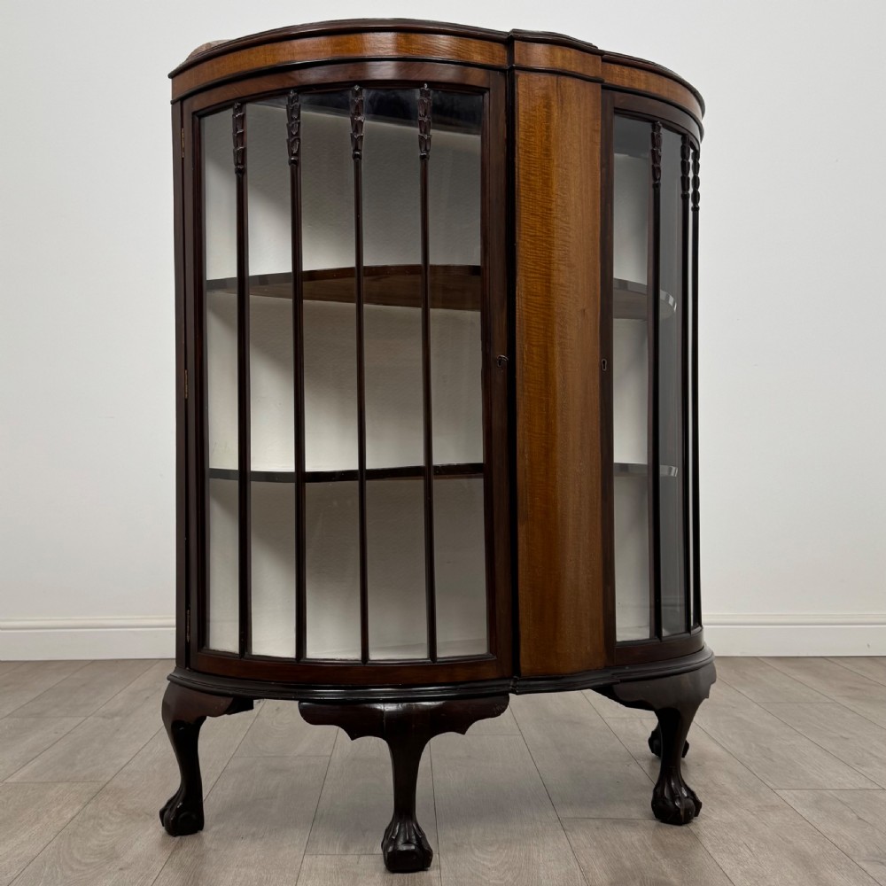 An early twentieth-century mahogany bow-front display cabinet featuring curved glass doors, vertical glazing bars, internal shelves, and cabriole legs with ball-and-claw feet. View IX