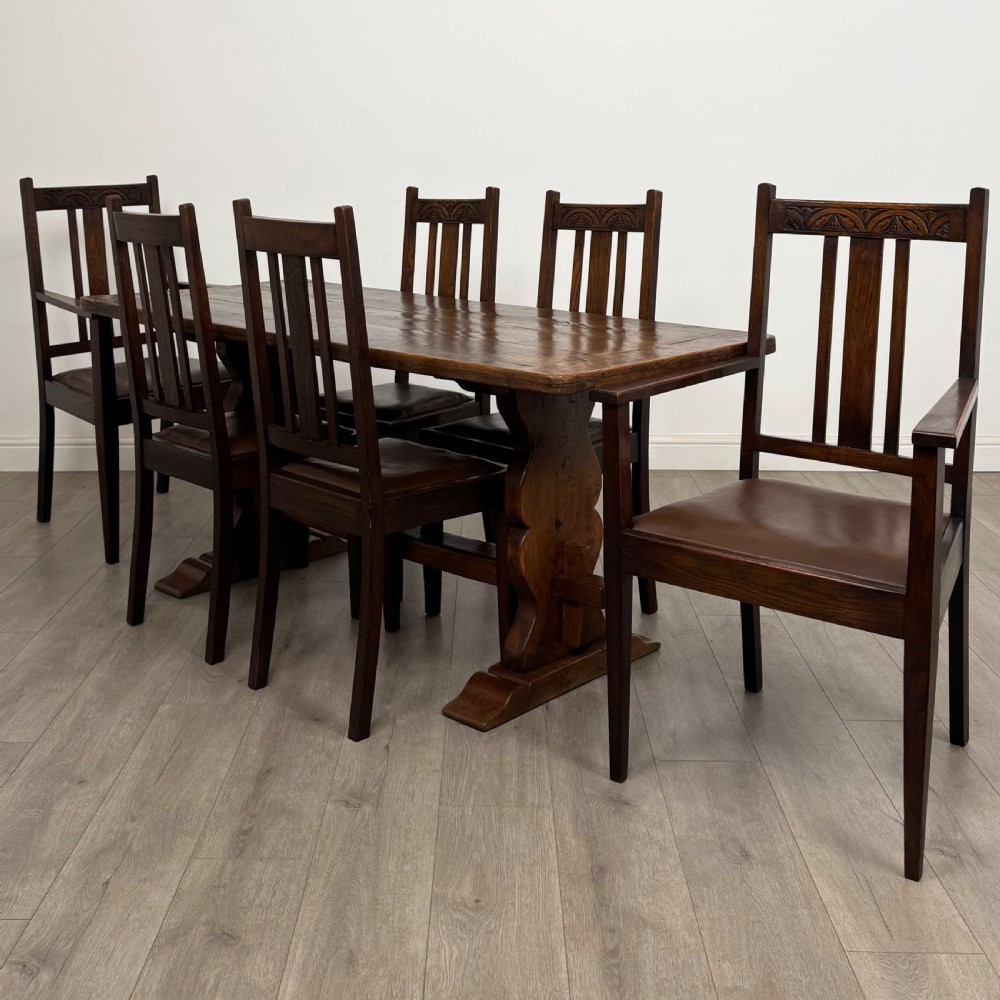 Dark oak trestle dining table paired with six matching carved oak chairs with dark leather seats.