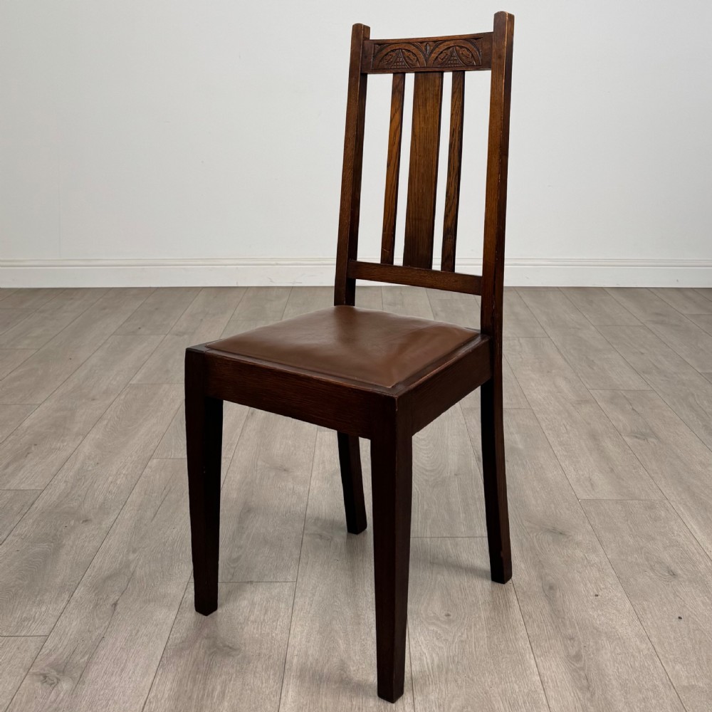 Dark oak trestle dining table paired with six matching carved oak chairs with dark leather seats. View IV